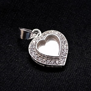 May include: A silver heart-shaped pendant with a clear crystal border. The pendant has a smooth, polished finish and is perfect for adding a touch of elegance to any jewelry collection.