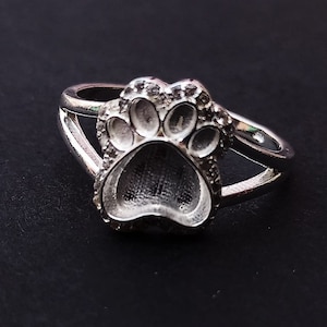 Op de afbeelding: Een zilveren ring met een pootprint ontwerp. De pootprint is gedetailleerd en heeft een textuur.
