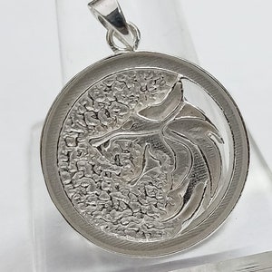 May include: Silver pendant featuring a detailed, textured design of a dragon with its wings spread. The pendant is round and has a smooth, polished edge.