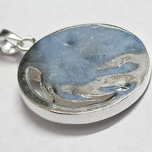May include: Silver pendant with a circular design. The pendant has a smooth, shiny surface and a cut-out design in the center.