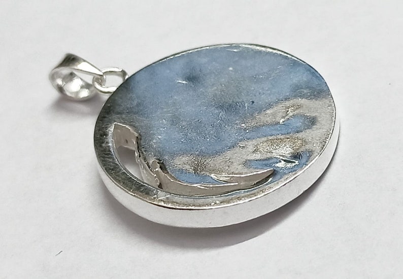 May include: Silver pendant with a circular design. The pendant has a smooth, shiny surface and a cut-out design in the center.