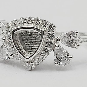 May include: A silver ring with a triangular setting surrounded by small clear stones. The ring has three pear-shaped stones on the side.