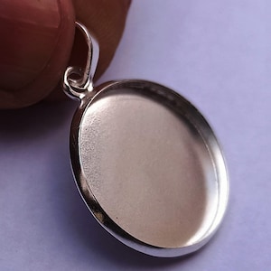 Può includere: Ciondolo in argento con una superficie rotonda, liscia e vuota. Il ciondolo ha un anello nella parte superiore per attaccare una catena.