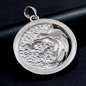 Puede incluir: Un colgante de plata con un diseño detallado de cabeza de lobo. El colgante es redondo y tiene una superficie texturizada. La cabeza del lobo está orientada hacia la derecha y tiene un diseño nítido y detallado.