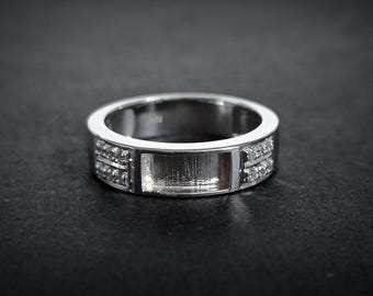 Op de afbeelding: Een zilveren ring met een rechthoekige inleg en kleine heldere stenen op de band.