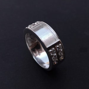 May include: A silver ring with a smooth, flat top and two rows of clear cubic zirconia stones around the band.