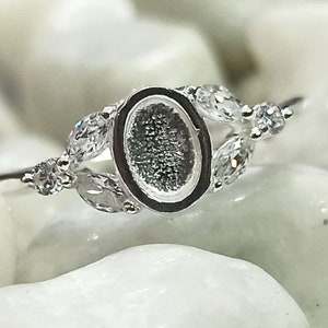 May include: Silver ring with an oval-shaped bezel and small clear stones set in leaf-shaped designs.