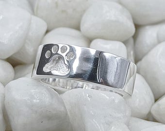Op de afbeelding: Een zilveren ring met een pootprint ontwerp. De ring is breed en heeft een gepolijste afwerking.