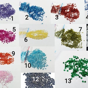 K&ouml;nnte beinhalten: Dreizehn kleine Beutel mit bunten, diamantf&ouml;rmigen Strasssteinen, nummeriert von 1 bis 13. Die Strasssteine sind in verschiedenen Farben, darunter lila, blau, rot, gelb, gr&uuml;n, orange und klar.