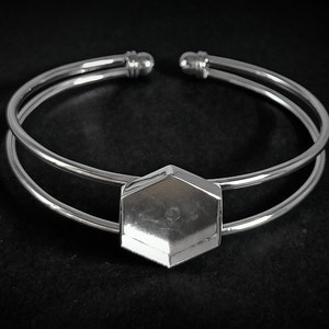May include: A silver double-band bangle bracelet with a hexagonal-shaped charm in the center.