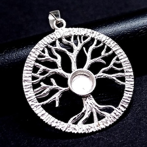 May include: Silver pendant featuring a detailed tree of life design with a round, open space in the center for a stone or charm. The pendant is circular and has a textured edge.