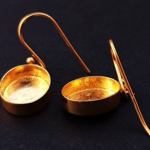 May include: A pair of gold-toned earring settings with a smooth, oval-shaped base and a hook closure.