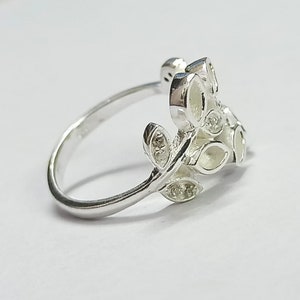K&ouml;nnte beinhalten: Ein silberner Ring mit einem zarten Blattdesign. Die Bl&auml;tter sind detailliert und mit kleinen, klaren Steinen besetzt.