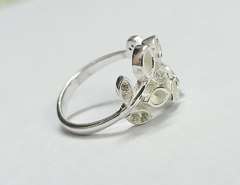 K&ouml;nnte beinhalten: Ein silberner Ring mit einem zarten Blattdesign. Die Bl&auml;tter sind detailliert und mit kleinen, klaren Steinen besetzt.