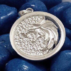 May include: A silver pendant featuring a detailed wolf head design. The pendant is round and has a textured surface.