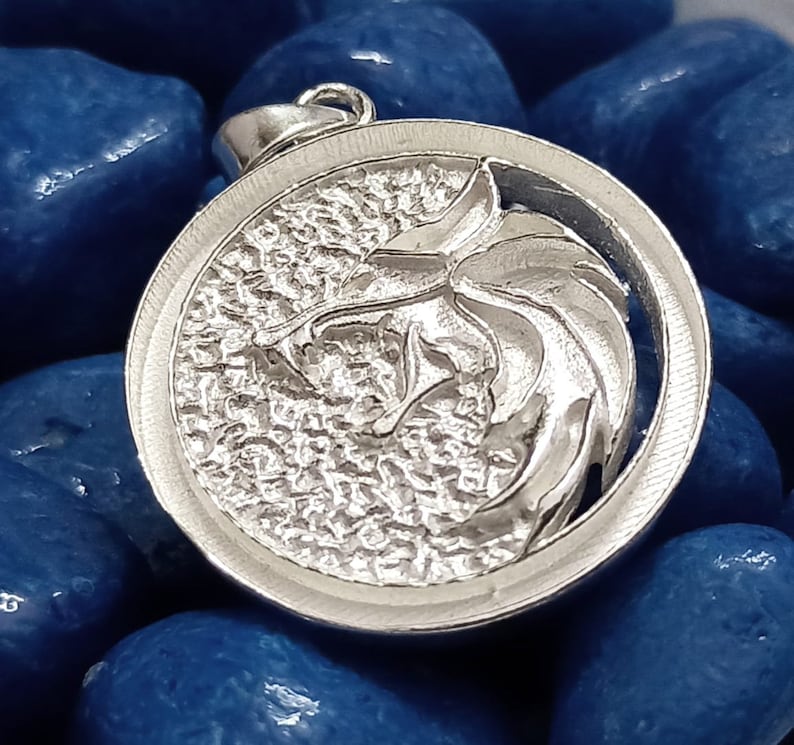 May include: A silver pendant featuring a detailed wolf head design. The pendant is round and has a textured surface.