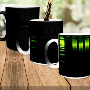 Puede incluir: Tres tazas negras con un diseño sensible al calor. Las tazas están vacías, pero cuando se vierte líquido caliente en ellas, aparece una imagen verde de un experimento de electroforesis en gel.