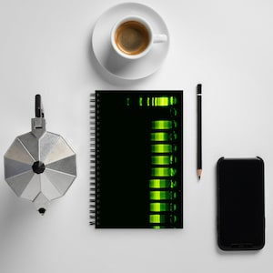 May include: A black spiral-bound notebook with a neon green design, a cup of espresso, a silver stovetop espresso maker, a black pencil, and a smartphone on a white surface. The notebook's design features a series of horizontal green bars.