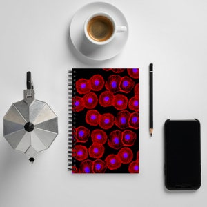 Könnte beinhalten: Ein schwarzes Spiralnotizbuch mit einem roten und blauen Zellmuster. Das Notizbuch liegt auf einer weißen Oberfläche mit einer Kaffeetasse, einem Bleistift und einem schwarzen Smartphone.