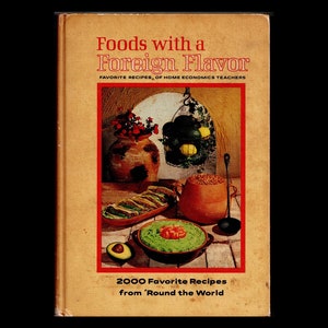 May include: A vintage cookbook titled "Foods with a Foreign Flavor" with a colorful illustration of a bowl of guacamole, a plate of tacos, and a pot of beans. The book cover also features the text "2000 Favorite Recipes from 'Round the World".