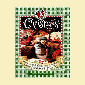May include: A Gooseberry Patch Christmas Book 3 publication featuring a green plaid border and a central image of a jar of hot chocolate mix, holiday decorations, and the text: Delicious, old-fashioned recipes, handmade holiday gifts & ideas for frosty fun!
