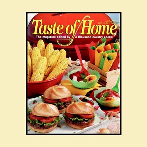 May include: A Taste of Home magazine cover featuring a red grill, a bowl of yellow corn on the cob, three hamburgers with lettuce and tomato on a strawberry-patterned tray, and small bowls of dessert with red sauce and green plastic spoons.