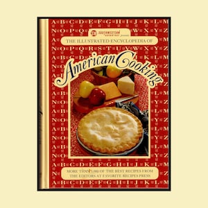 May include: A hardcover book titled The Illustrated Encyclopedia of American Cooking with a red cover featuring a repeating alphabet pattern. The front cover displays a photograph of a baked pie, a red apple, cheese, and a basket of fruit.