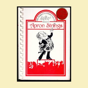 May include: A spiral-bound cookbook titled Apron Strings, presented by The Women's Committee of the Richmond Symphony. The white cover features a red border and a black-and-white illustration of a conductor wearing a piano-key apron.