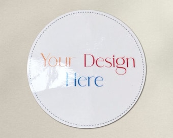 May include: A white round sticker with a dotted border. The sticker has the text "Your Design Here" in red, orange, and blue.