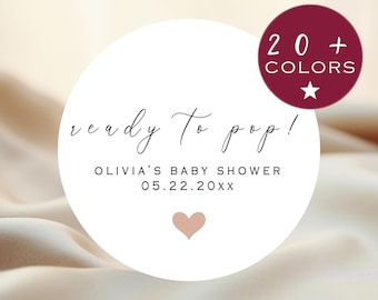 May include: White circle sticker with the text "ready to pop!" and "Olivia's Baby Shower 05.22.20XX". A small pink heart is below the text. A burgundy circle with white text "20+ COLORS" and a white star is in the upper right corner.