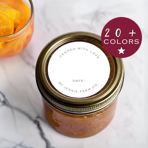 Peut inclure: Un pot en verre rempli d'une confiture orange clair, surmonté d'un couvercle doré et d'une étiquette blanche. L'étiquette indique "Canned with Love", "Date:" et "By Jennie Farm Co." Un cercle bordeaux avec le texte "20+ COLORS" est en haut à droite.