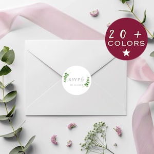 May include: A white envelope with a round sticker that says "RSVP by" and the date 06.22.20xx, surrounded by green leaves. A burgundy circle with the text "20 + COLORS" is in the upper right corner. The image is decorated with pink flowers and a pink ribbon.