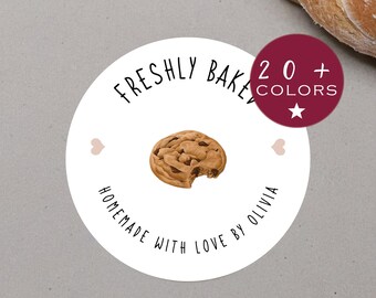 Puede incluir: Pegatina redonda con fondo blanco y texto negro que dice "Freshly Baked Homemade with Love by Olivia". En el centro de la pegatina hay una galleta de chocolate con chispas marrón con un mordisco. Hay dos pequeños corazones rosas a cada lado de la galleta. En la esquina superior derecha de la pegatina hay un círculo granate con una estrella blanca y texto blanco que dice "20+ Colores".