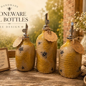May include: Handmade stoneware oil bottles with a bee design. The bottles are yellow with black bee illustrations and silver spouts. Each bottle has a tag tied with twine. A small framed sign is also present.
