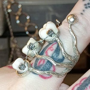 Puede incluir: Un anillo plateado con un diseño floral con detalles en blanco y negro. El anillo tiene un estilo único y artístico, con un grupo de pequeños elementos en forma de flor. El anillo se lleva en un dedo.