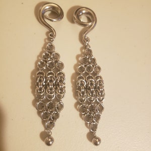 May include: A pair of silver metal earrings with a spiral design at the top and a chain-like design hanging down. The chain-like design has a ball at the bottom.