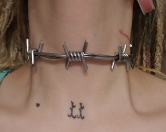May include: A silver barbed wire choker necklace. The necklace is made of metal and has a sharp, edgy look.