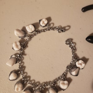 Charmer. Faux human teeth charm bracelet on heart base.