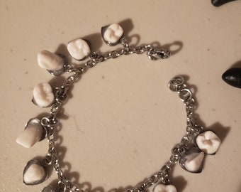 Charmer. Faux human teeth charm bracelet on heart base.