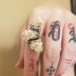 Puede incluir: Un anillo de plata con tres dientes blancos engastados en un diseño floral.