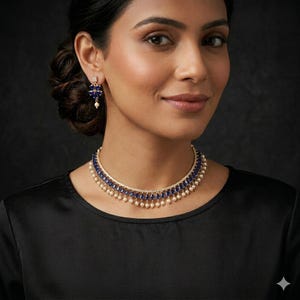Puede incluir: Un collar dorado y pendientes a juego. El collar presenta una fila de piedras preciosas azules y pequeñas perlas blancas. Los pendientes tienen un diseño similar con piedras azules y una sola perla. La joyería se usa sobre un fondo negro.
