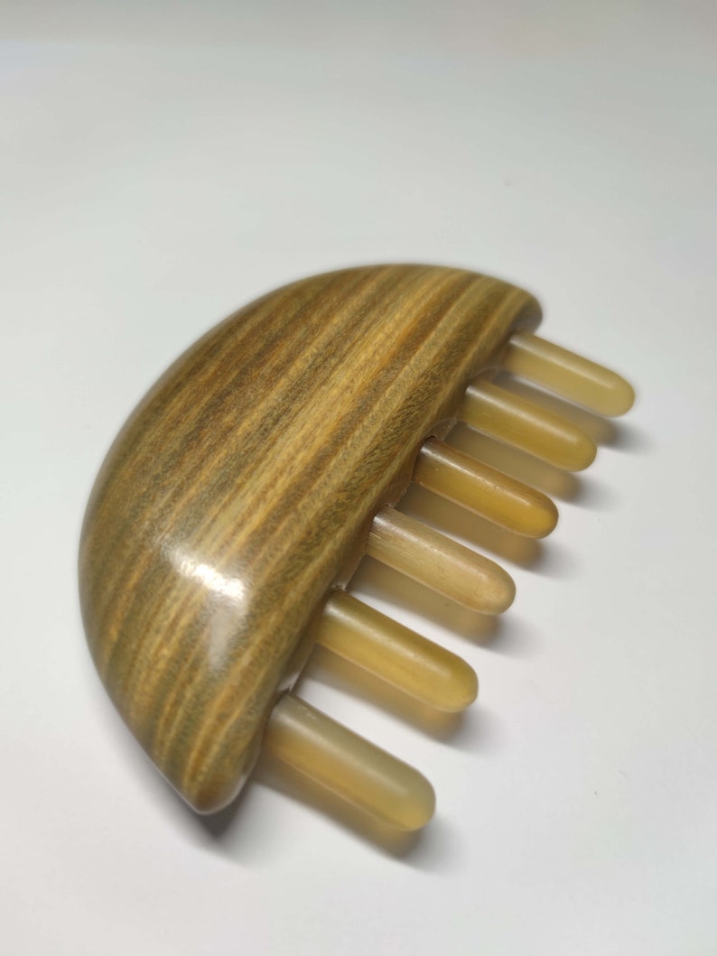 May include: A wooden hair comb with a half-moon shaped base and a row of beige teeth. The wood has a brown and green striped pattern.