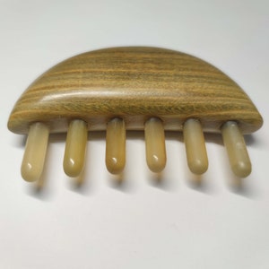 May include: A wooden comb with five beige teeth. The comb is shaped like a half-circle and has a wood grain pattern.