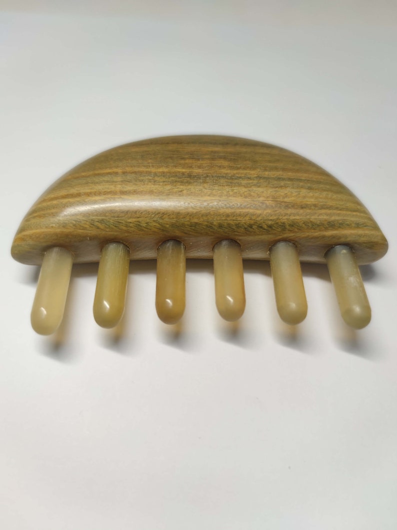 May include: A wooden comb with five beige teeth. The comb is shaped like a half-circle and has a wood grain pattern.