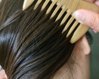 May include: A wooden comb with a curved handle and fine teeth. The comb is being used to brush a person's dark brown hair.