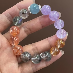May include: A gemstone bracelet with a variety of coloured beads. The bracelet includes clear, orange, purple, and blue beads. The beads are round and appear to be made of polished stone, strung together on a stretchy cord.