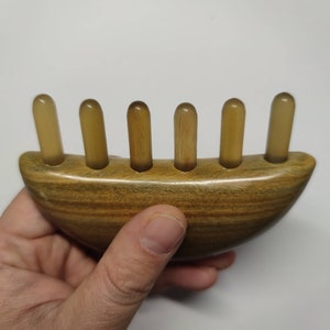 May include: A wooden comb with five rounded teeth, designed for scalp massage. The comb is brown with a natural wood grain and has a curved shape.
