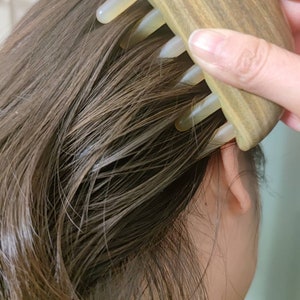 May include: A brown and beige wooden hair comb with five teeth. The comb is shaped like a half-moon and has a smooth, polished finish.