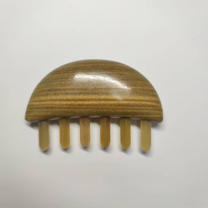 May include: A wooden hair comb with a half-circle shaped handle and five teeth. The handle is made of light brown wood with dark brown stripes. The teeth are made of a lighter brown wood.