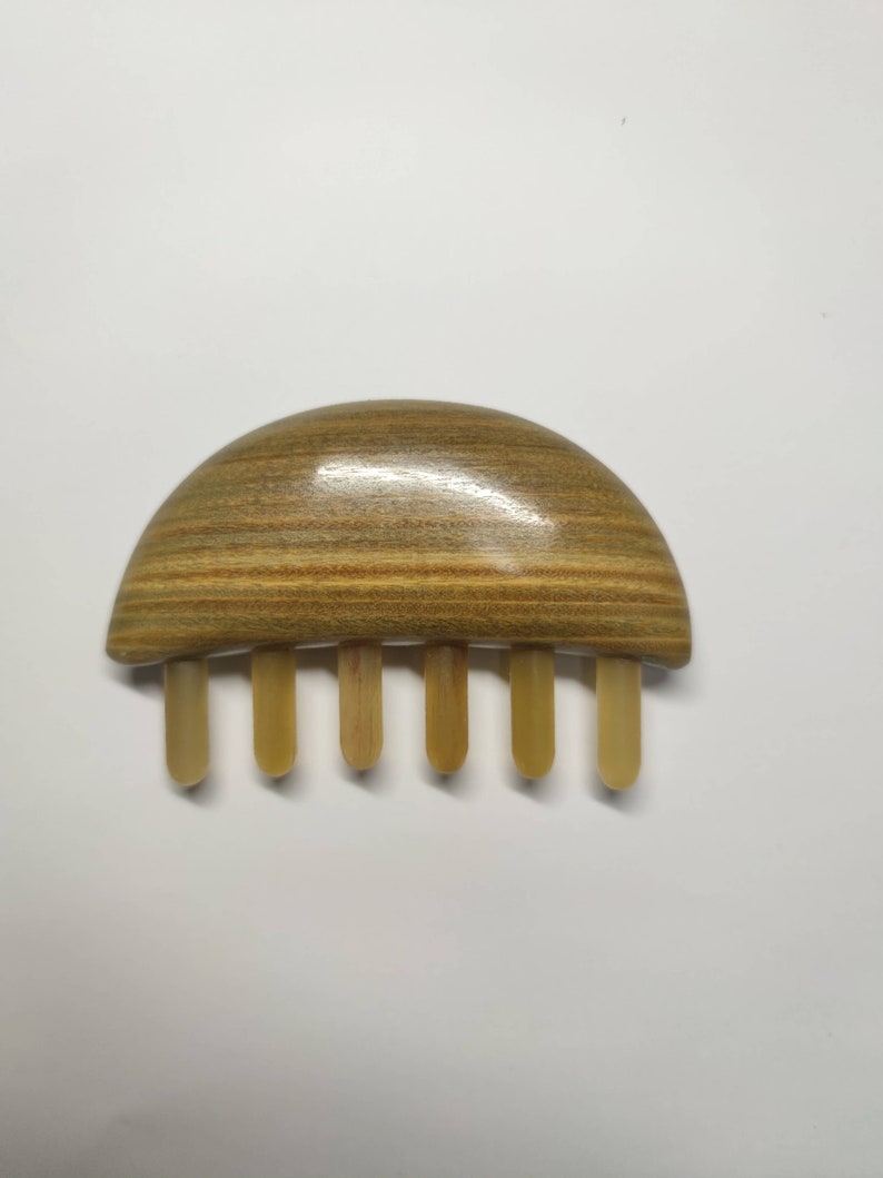 May include: A wooden hair comb with a half-circle shaped handle and five teeth. The handle is made of light brown wood with dark brown stripes. The teeth are made of a lighter brown wood.